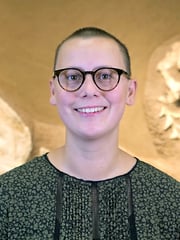 Porträtfoto einer Frau mit kurzen Haaren und Brille vor einem Dinosaurer-Fossil im Hintergrund